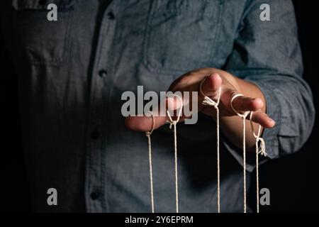 Nahaufnahme von man steuert die Puppe mit den Fingern. Man`s Hand steuert die Puppe mit den Fingern, die an Threads vor schwarzem Hintergrund befestigt sind, Manipul Stockfoto